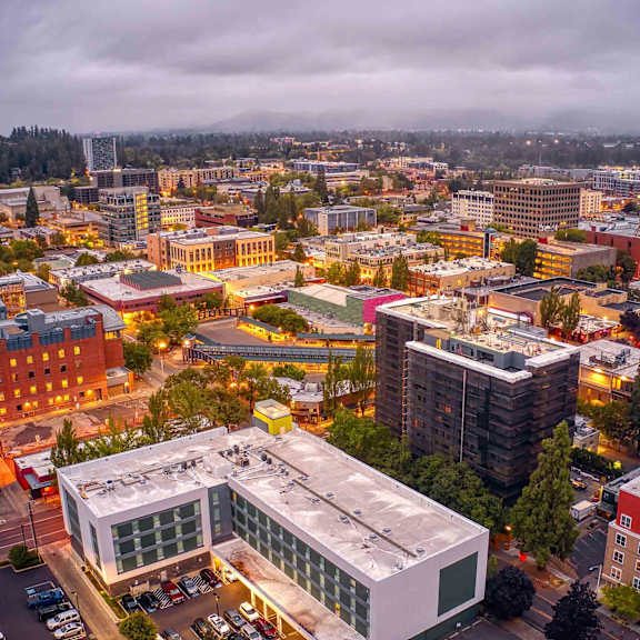 Eugene, Oregon, cityscape with a large white building in the foreground and a cloudy sky above.