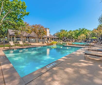A large swimming pool surrounded by trees and lounge chairs.
