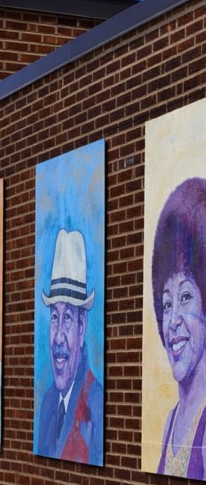 A row of portraits are displayed on a brick wall.
