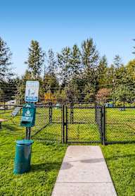 A park with a sign, a fire hydrant, and a trash can.