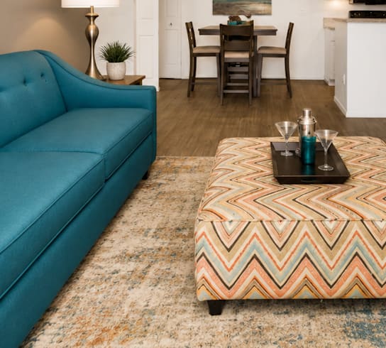 A living room with a blue couch and a chevron patterned ottoman.