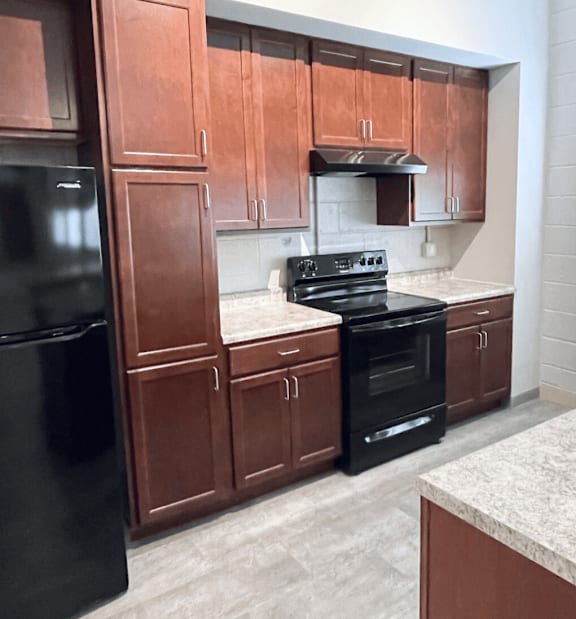 A kitchen with brown cabinets and a black refrigerator.
