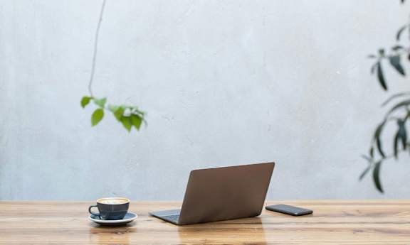 A laptop is open on a wooden table with a cup on it.