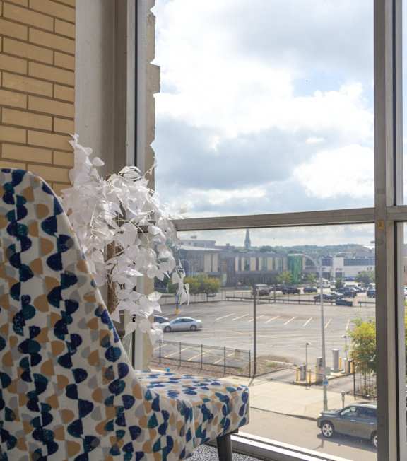 A chair with a blue and yellow pattern is in front of a window with a view of a parking lot and buildings.