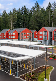 A series of red buildings with white roofs are surrounded by trees and a parking lot with solar panels.