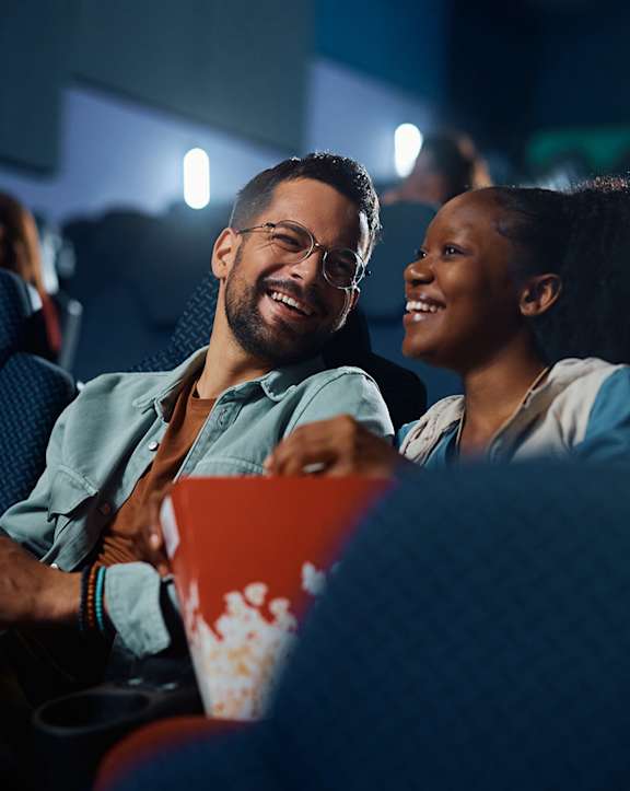 A man and a woman are laughing while watching a movie in a theater.