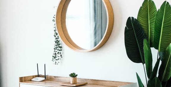 Bedroom with a round mirror on the wall. A long white and wooded dresser is below it. A green tall plant is to the right of the dresser. 