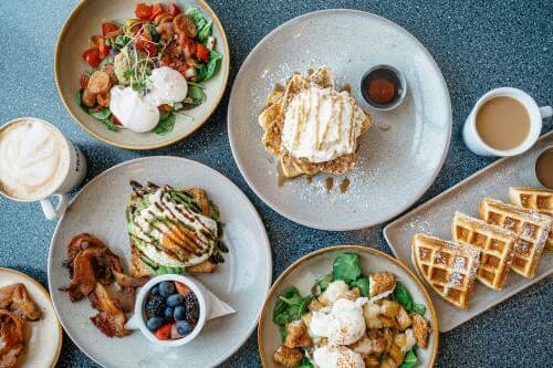 a table topped with plates of breakfast food and waffles