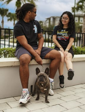 man and woman with a dog siting on a wall beside the fenced in pool