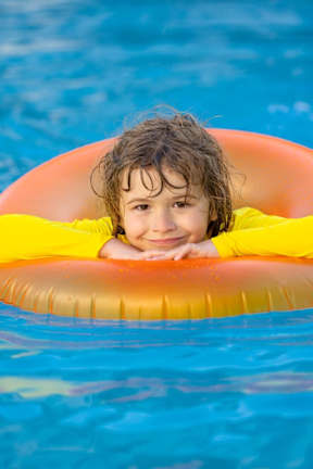 A child is floating on an orange and yellow float in a blue pool.