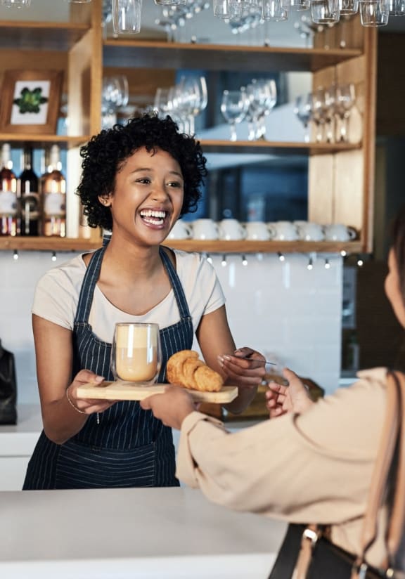 Woman Smiling while Handing Woman Coffee and Pastries