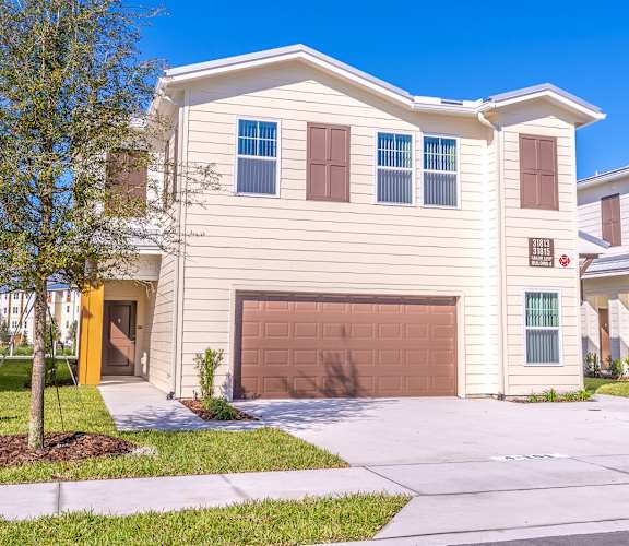 A house with a brown garage door is surrounded by other similar houses.