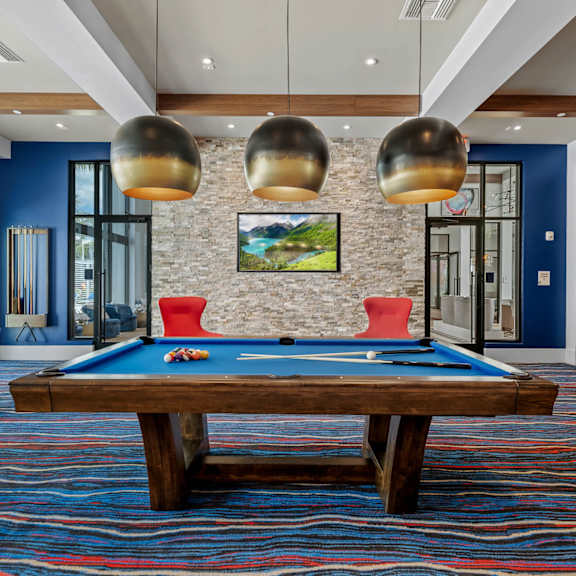A pool table with a red cloth and a picture of a landscape hanging on the wall above it.