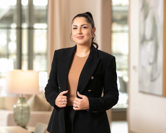 A woman in a black suit stands in a well-lit room.