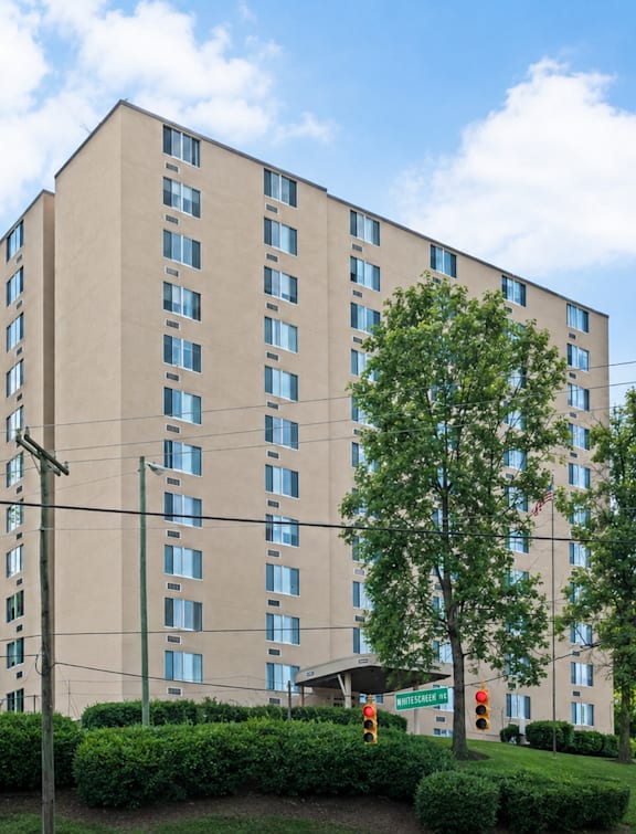 A large beige building with many windows and trees in front.