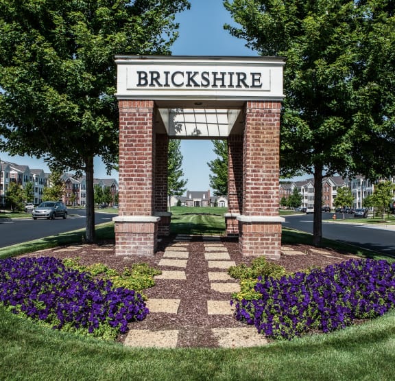 an architectural brick monument with a sign on top of a flower garden  at Brickshire Apartments, Indiana