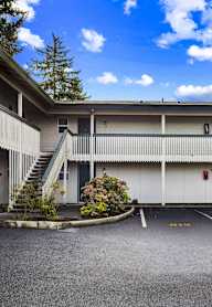 A parking lot in front of a white building with green doors.