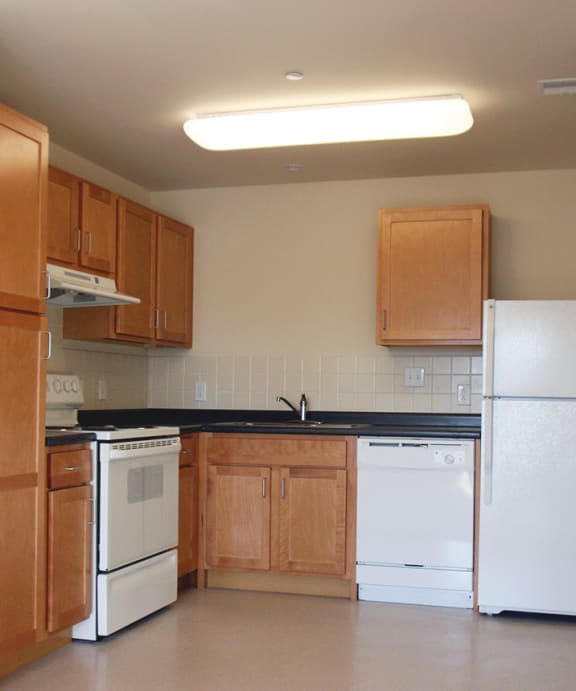 An empty kitchen with wood cabinets and white appliances at Fairfield apartments and townhomes in Pittsburgh, PA