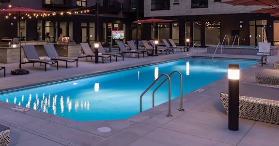 A swimming pool surrounded by lounge chairs and umbrellas in a courtyard.
