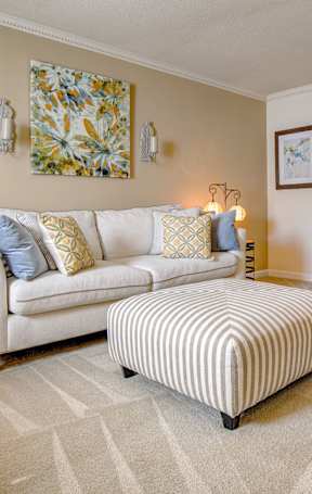 A living room with a white couch and a striped ottoman.