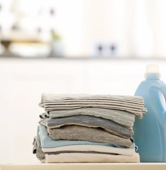 a pile of folded laundry on a shelf with a blue detergent bottle