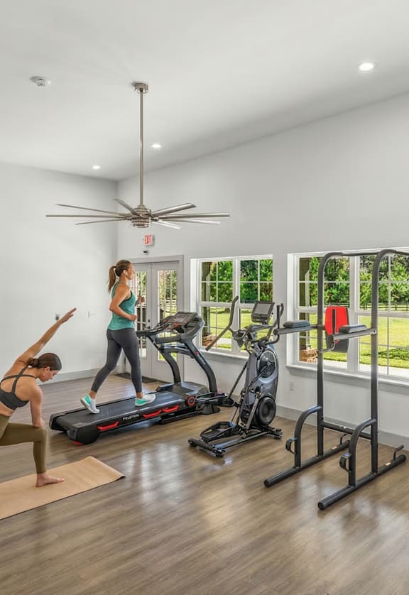 A woman is exercising in a spacious gym with a treadmill, exercise bike, and other equipment.
