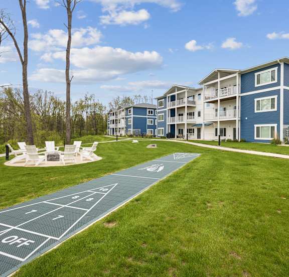 A blue and white apartment building with a green lawn and a shuffleboard court.