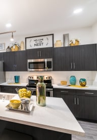 Kitchen with a ceiling light and hallway and island and stools and cabinets and  fridge and oven and stove and microwave