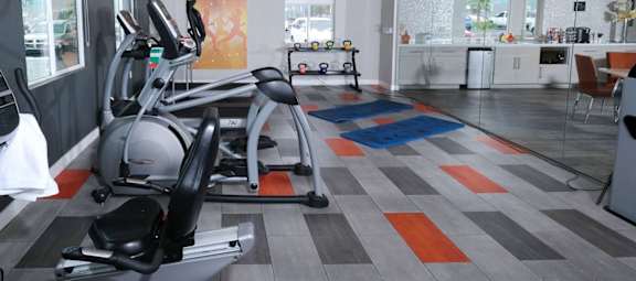 Fifteen 50 apartments near Las Vegas strip on site fitness center with modern orange and grey tile floor and exercise equipment facing wall TVs.