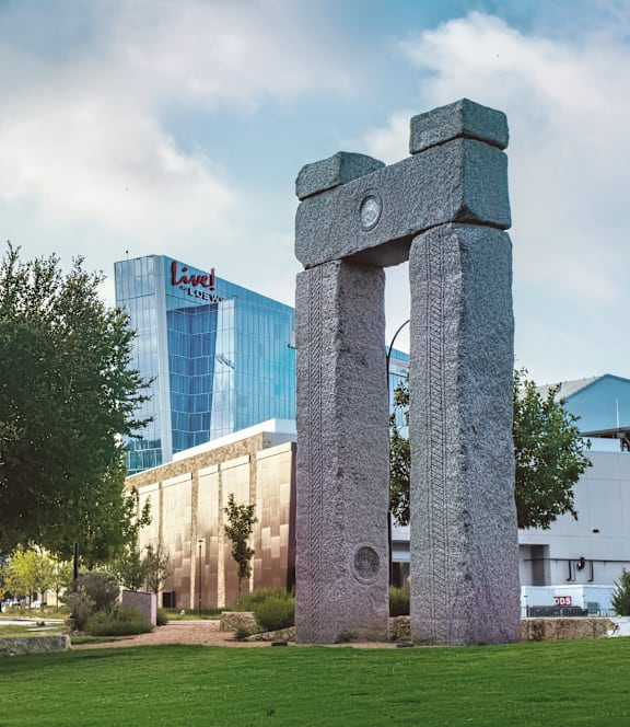 A large stone structure stands in a grassy field with a modern building in the background.