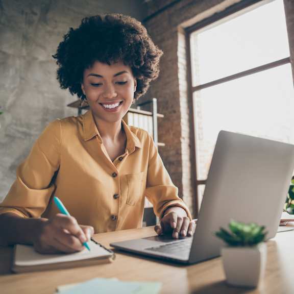 A person is writing in a notebook while using a laptop.