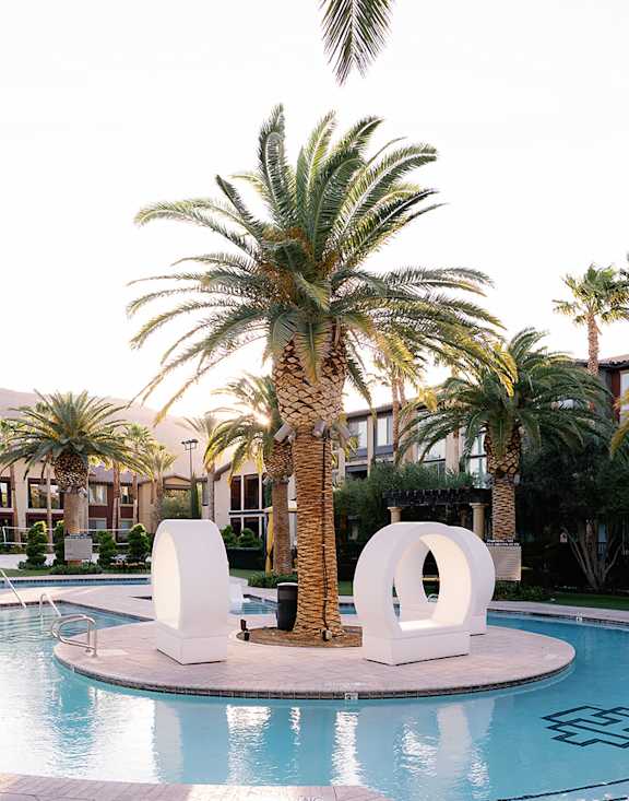 A pool surrounded by palm trees and a white sculpture.