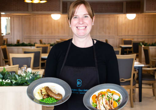 a woman in an apron holding two plates of food