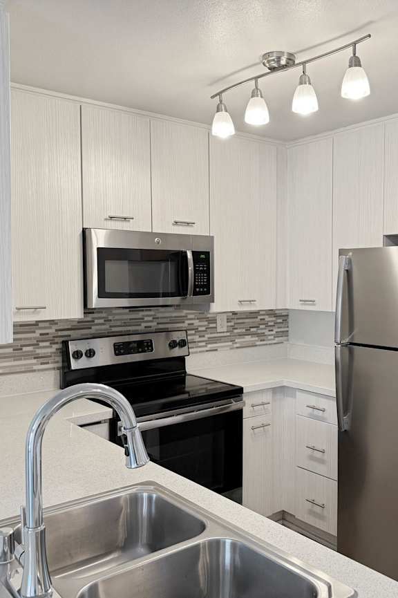 A kitchen with a stainless steel refrigerator and a sink with a faucet.