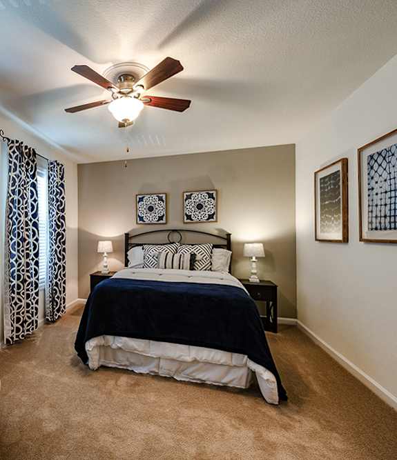 A bedroom with a bed, chair, and ceiling fan.