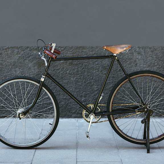 A black bicycle with a brown seat is leaning against a grey wall.