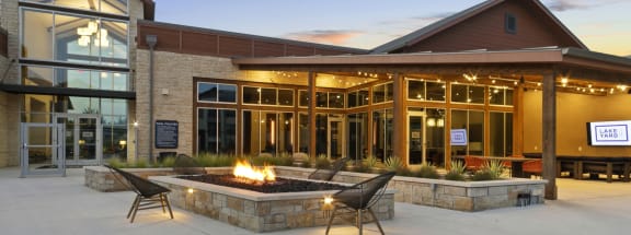a patio with a fire pit and chairs in front of a building