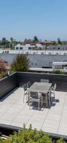 A rooftop patio with a table and chairs overlooks a cityscape.