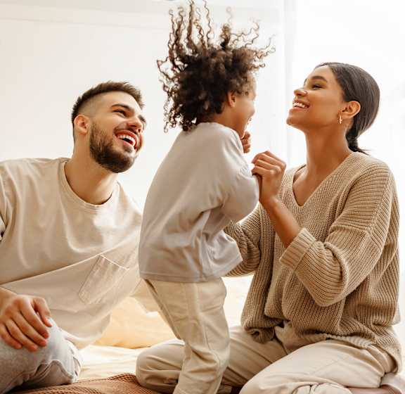 A family of three is having a joyful moment on a bed.