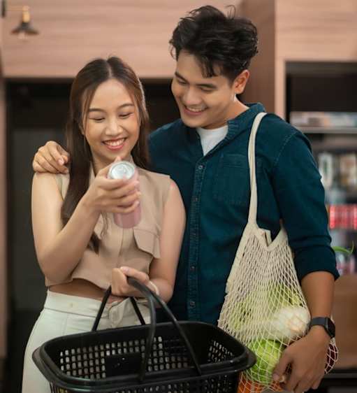 A man and a woman are shopping together, with the woman holding a smartphone and the man holding a shopping bag.