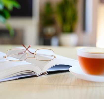 A pair of glasses rests on an open book next to a cup of tea.