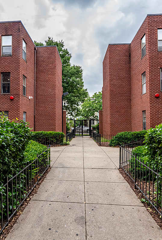 a walkway between two brick apartment buildings with a sidewalk