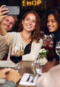 A group of people are sitting around a table taking a selfie.