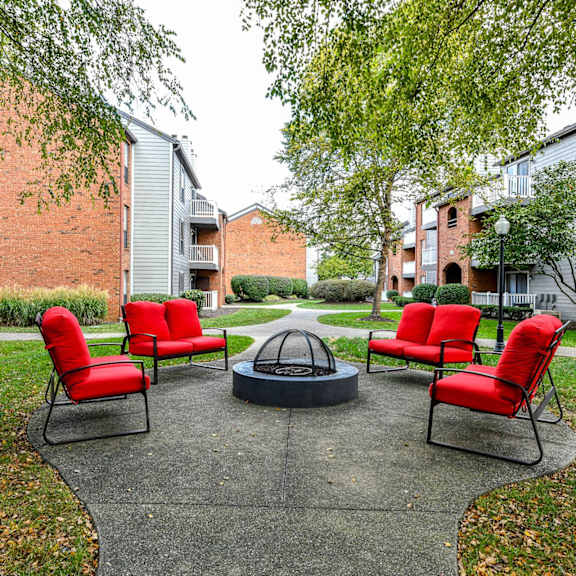 A small garden with a fire pit and four red chairs.