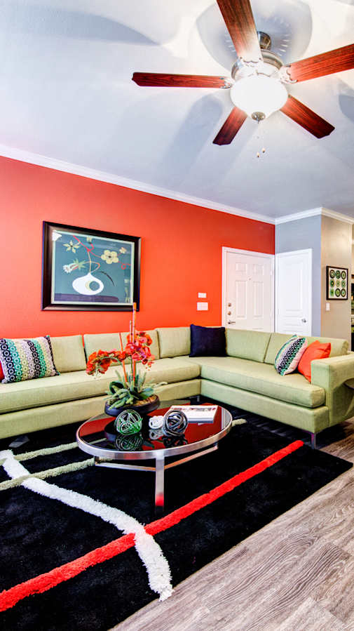 A living room with a green couch and a red wall.