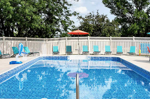 a swimming pool with chairs and umbrellas in front of a fence