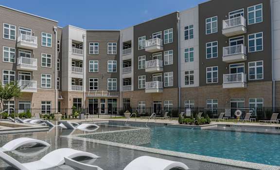 a swimming pool with two white chairs in front of an apartment building