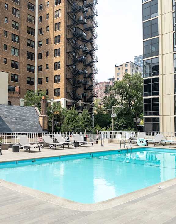 A swimming pool surrounded by lounge chairs and buildings in the background.