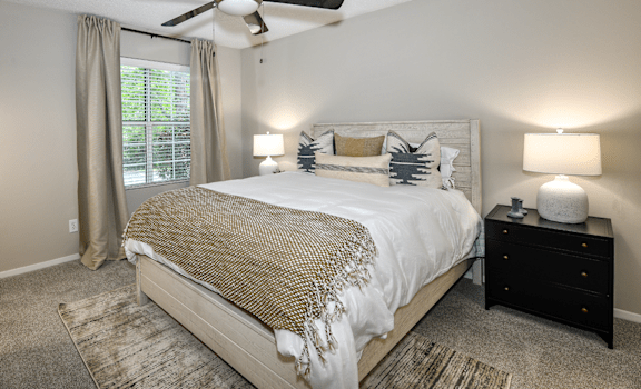 A bedroom with a large bed, a ceiling fan, and a nightstand with a lamp.