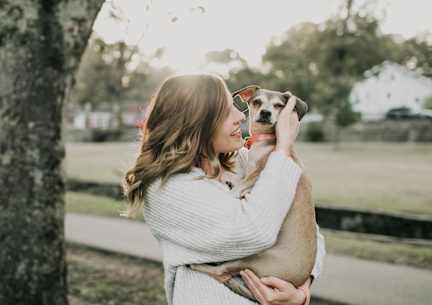 A woman in a white sweater is hugging a dog in a park.